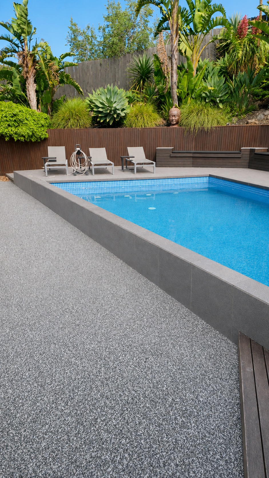 Resin bound pool surround in grey aggregate beside a tiled pool with landscaped tropical garden